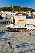 Tourists in St. Stephens Square, with the Spanish Fort (Fortica) above, Hvar Town, Hvar Island, Dalmatian Coast, Croatia, Europe