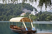 Oars on traditional wooden pletnja rowing boat moored by jetty and St Martin's Roman Catholic Church across the lake, Lake Bled, Bled, Slovenia, Europe