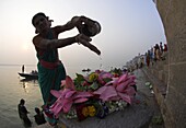 Woman pouring water over flowers on an altar as a religious ritual, Kedar Ghat, Varanasi, Uttar Pradesh state, India, Asia