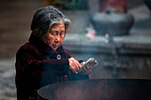 Ältere Frau verbrennt falsche Banknoten als Gabe im Tempel Jade Buddha, Shanghai, Shanghai, Asien