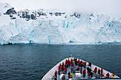 Passengers on bow of expedition cruise ship MS Hanseatic (Hapag-Lloyd Cruises) with 40-60 meter glacier wall, Paradise Bay (Paradise Harbor), Danco Coast, Graham Land, Antarctica