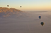 Hot air balloons on an excursion flying over the desert early morning at dawn , sunrise, on the West bank of the river Nile near Luxor, Egypt, North Africa, Africa