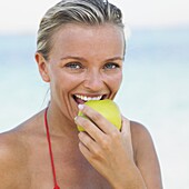 Woman in bikini on beach holding apple