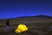 Hiker and tent illuminated under the night sky, Great Sand Dunes National Park, Colorado, United States of America, North America