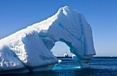 Looking through an Antarctic iceberg arch to the Akademik Ioffe research ship on the horizon, Antarctica, Polar Regions