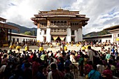 View over crowds of spectators to the main courtyard during a masked dance by Buddhist monks at Gangtey Tsechu at Gangte Goemba, Gangte, Phobjikha Valley, Bhutan, Asia