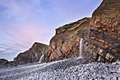 Sandstone rock strata and waterfalls at Sandymouth Beach at sunset, near Bude, Cornwall, England, United Kingdom, Europe