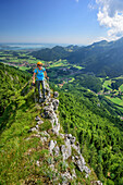 Woman hiking walking on small ridge, lake Chiemsee in background, Zellerhorn, Chiemgau Alps, Upper Bavaria, Bavaria, Germany