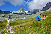 Frau beim Bergsteigen liegt in Wiese, Großglockner im Hintergrund, Großglockner, Hohe Tauern, Osttirol, Österreich