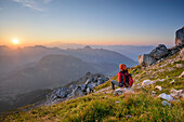 Woman hiking looking towards sunrise above Mont Blanc range, La Tournette, Haute-Savoie, France