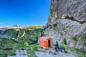 Zwei Personen stehen vor Biwak Zeni, Langkofel im Hintergrund, Bivacco Zeni, Vallacciagruppe, Marmolada, Dolomiten, UNESCO Weltnaturerbe Dolomiten, Trentino, Italien