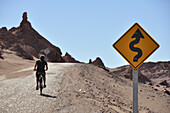 Man cycling and crossing traffic sign at road, Valle de la Luna, Valley of the moon, Atacama desert, Reserva Nacional Los Flamencos, Region de Antofagasta, Andes, Chile, South America