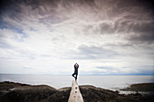 A young woman does the Yoga Tree Pose while balancing on a log at the beach  near Sechelt, BC, Canada.