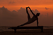 Mädchen macht Yoga bei Sonnenuntergang am Strand von Sri Lanka