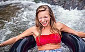 A young woman laughs while tubing down rapids on a river.