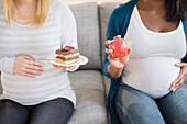 Pregnant women comparing apple and cake on sofa