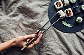 Hand of woman reaching for platter of sushi on bed