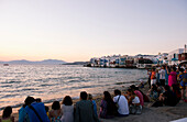 Tourists gathered along the seafront in the Little Venice area of Mykonos Town to watch the sunset, Mykonos, Cyclades, Greek Islands, Greece