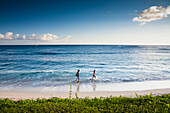 'A couple walks along the popular tourist beach; Poipu, Kauai, Hawaii, United States of America'