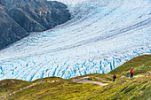 A man and woman hiking down the Harding Icefield Trail with Exit Glacier in the background, Kenai Fjords National Park, Kenai Penninsula, Southcentral Alaska