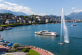 bateau de croisiere passant a proximite du jet d'eau de lugano avec la ville en fond, lugano, tessin, suisse