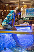 child with the feet in an aquarium of dead skin cleaning fish (fish pedicure), asiatique the riverfront, bangkok, thailand, asia