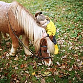 A little girl kissing a pony while he is grazing