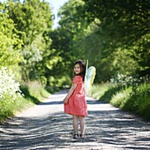 s A 5 years old girl wearing butterfly wings, in the countryside