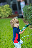 Caucasian baby boy playing with hose in backyard