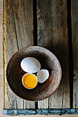 Yolk in Cracked Eggshell and Whole Egg in Bowl, High Angle View