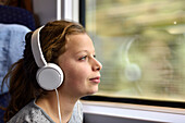 Girl listening to music with headphones in train, Germany, Europe