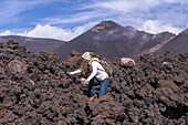 Abgekühltes Lavafeld des Etna Vulkans mit Lava-Flow des Südost Kraters im Hintergrund. Frau läuft über erkaltetes, scharfkantiges Lavafeld, Sizilien, Italien