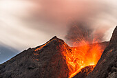 Große Eruption mit Lavaauswurf an der offenen Flanke des Vulkans Batu Tara in der Flores Sea bei Nacht mit Sternenhimmel und Vulkan-Gasen, Insel Komba, Flores Sea, Indonesien