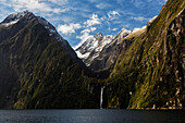 Waterfall from mountains over remote river, Milford Sound, Fiordland, New Zealand