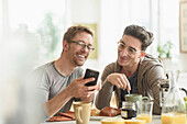 Caucasian gay couple using cell phone at breakfast