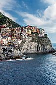 Buildings on rocky Manarola coastline and ocean, La Spezia, Italy