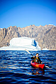 Woman paddling canoe near glaciers in remote river