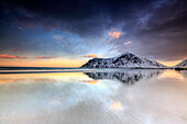 Sunset on Skagsanden beach surrounded by snow covered mountains reflected in the cold sea, Flakstad, Lofoten Islands, Arctic, Norway, Scandinavia, Europe