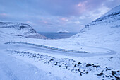 Snow covered road winding down between mountains near Nordradalur on the Island of Streymoy, Faroe Islands, Denmark, Europe