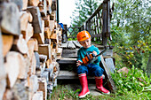 Junge, 4 Jahre, mit Spielzeug Motorsäge vor Alpinhütte, Feuerholz vor Alpenhütte, Maria Alm, Berchtesgadener Alpen, Österreich, Europa