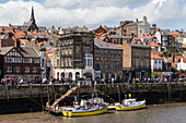 Boats moored on the West Side of the River Esk, with many passers-by on Pier Road, Whitby, North Yorkshire, Yorkshire, England, United Kingdom, Europe