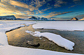 The golden sunrise reflected in a pool of the clear sea where the snow has melted, Haukland, Lofoten Islands, Arctic, Norway, Scandinavia, Europe