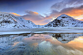 Sunrise on Uttakleiv beach surrounded by snow covered mountains reflected in the cold sea, Lofoten Islands, Arctic, Norway, Scandinavia, Europe