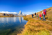 Hikers walking on the path beside the Stellisee with the Matterhorn reflected, Zermatt, Canton of Valais, Pennine Alps, Switzerland, Europe