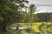 View on the river landscape and shore vegetation of the Spreewald Biosphere Reserve with oncoming kayak tourists from the water under overcast sky, biosphere reserve, Schlepzig, Brandenburg, Germany