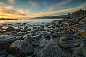 Woman sits on the shore of the Pacific Ocean watching the sunset near Jordan River, Vancouver Island, British Columbia, Canada