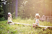 Girls playing telephone on wooden log in garden