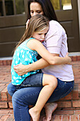 Close up of mother comforting daughter on front stoop