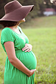 Pregnant Caucasian woman holding belly in field