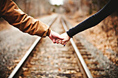 Close up of couple holding hands on railroad tracks